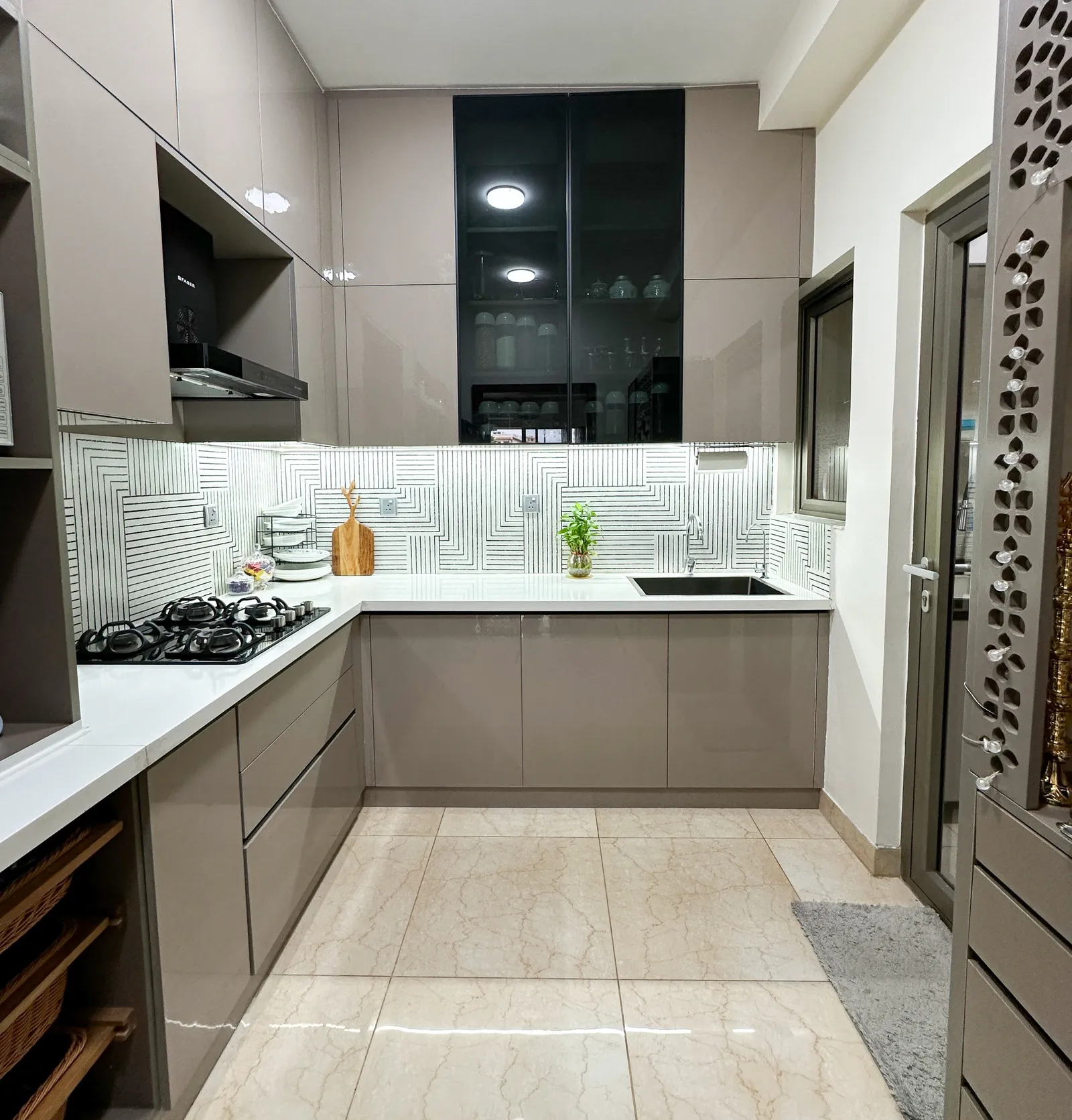 L-shaped kitchen with taupe cabinets and black glass tall unit — Somani's Residence
